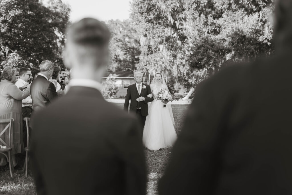 Bride walks toward groom, amidst wedding guest. 